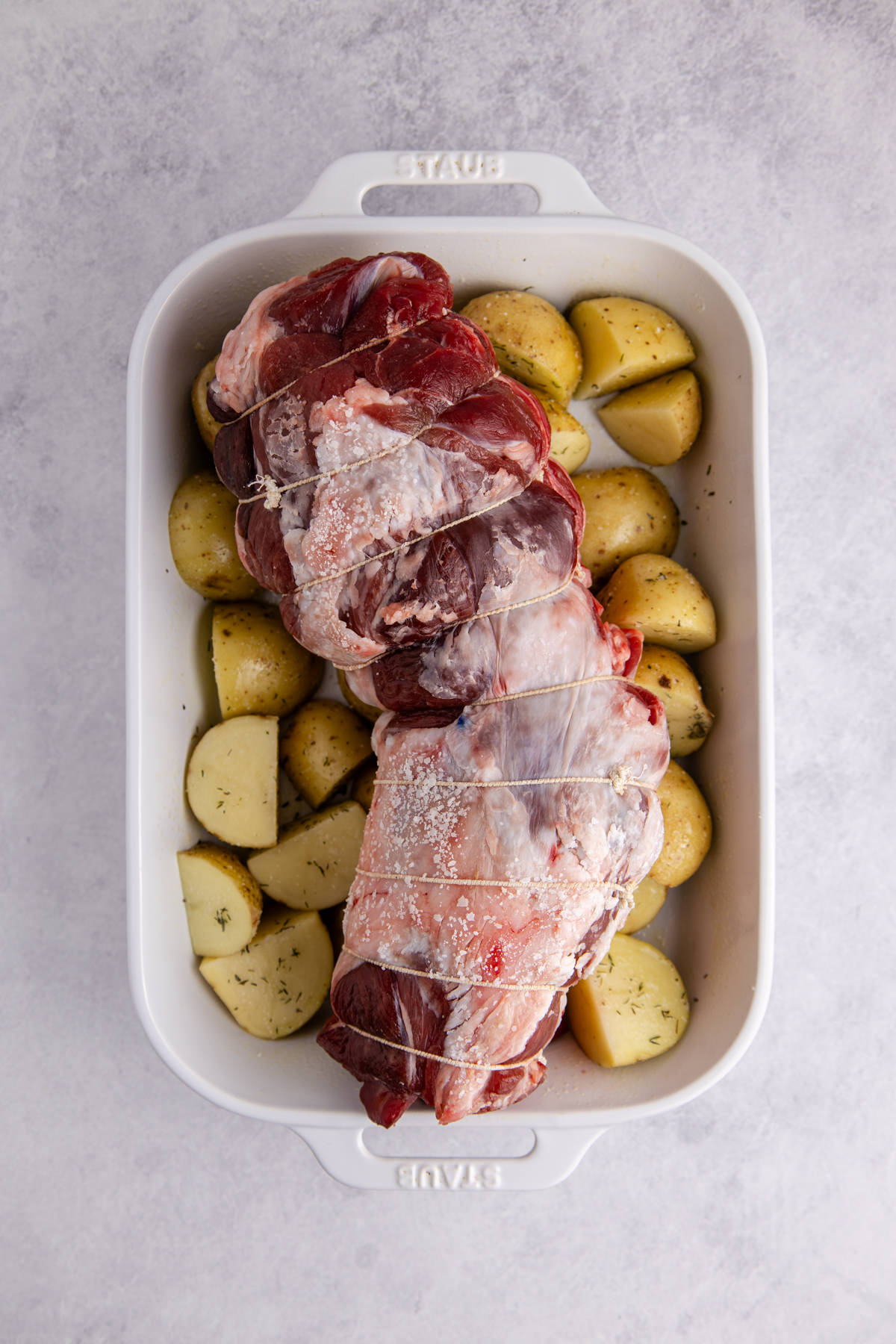 Lamb set on a roasting pan over potatoes basted with the garlic mixture.