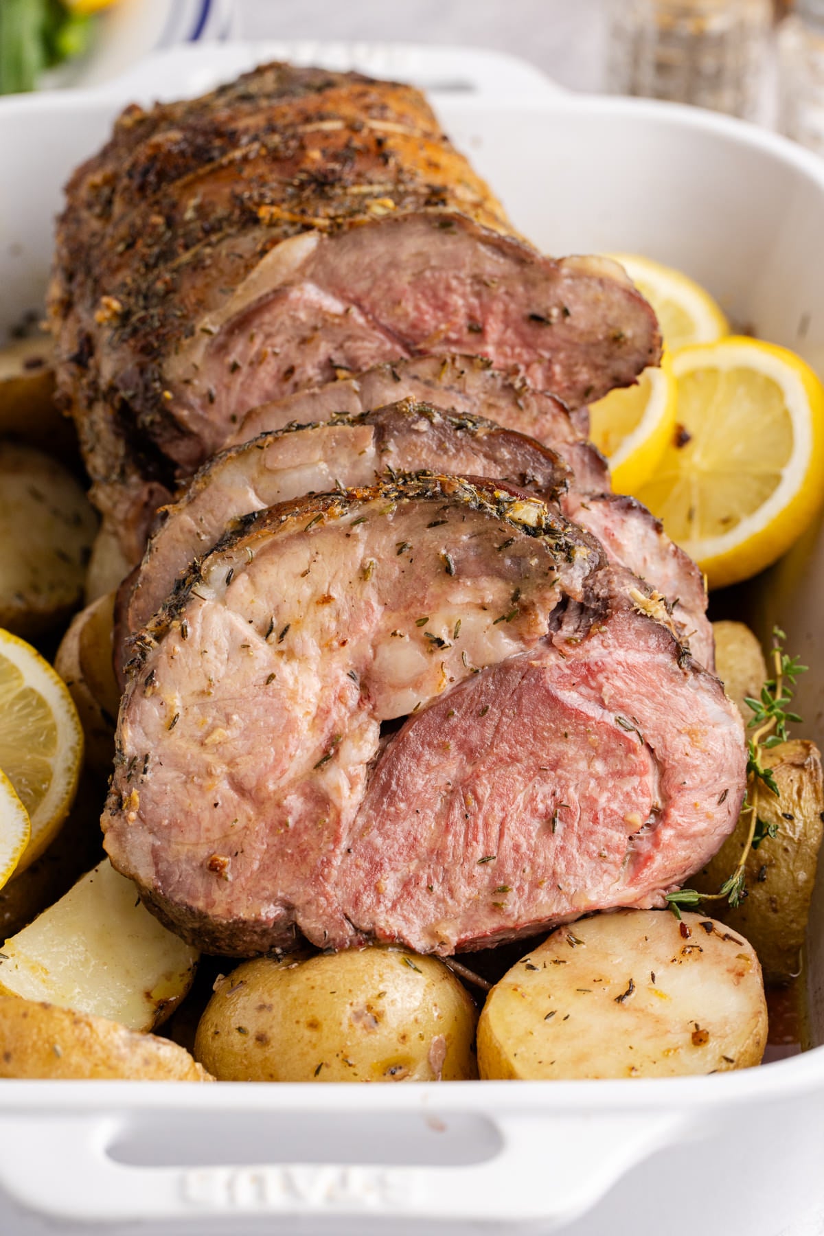 Boneless leg of lamb sliced over potatoes with some slices of lemon for garnish.