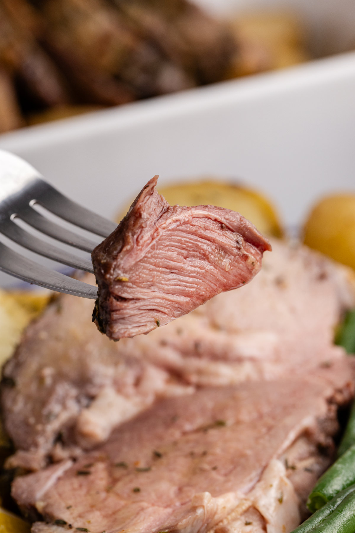 A piece of boneless leg of lamb on a fork in the air.