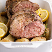 Boneless leg of lamb in a baking dish with potatoes and lemon slices.