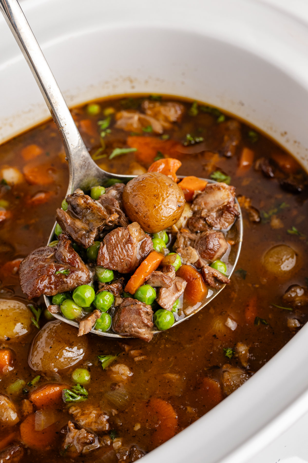 A ladle holding up stew with lamb and veggies.