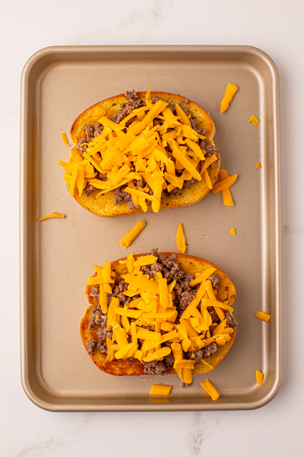 Cheese sprinkled on top of Texas toast with ground beef.