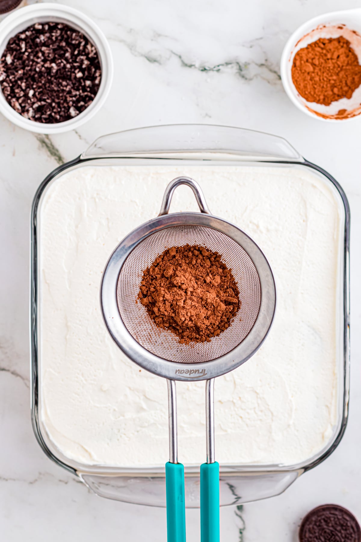 Sprinkling cocoa through a small sieve to distribute cocoa powder evenly on top.