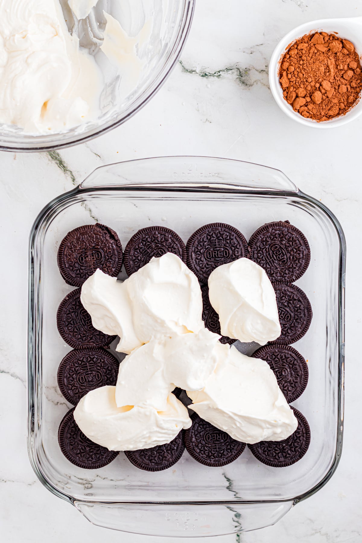 A layer of Oreos in a dish covered in dollops of marscapone layer.