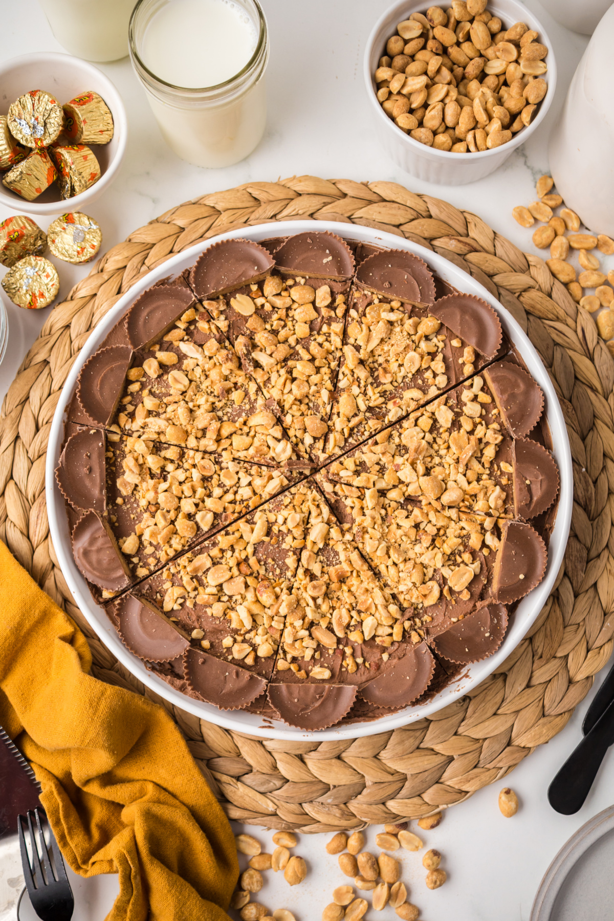 A whole pie covered with melted chocolate, crushed peanuts surrounded by reese's peanut butter cups.