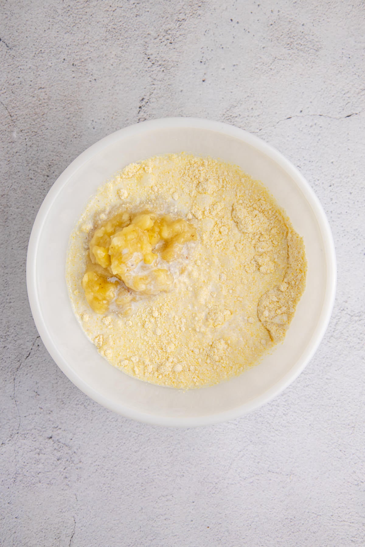 Dry cornbread ingredients with a spoonful of banana added. 
