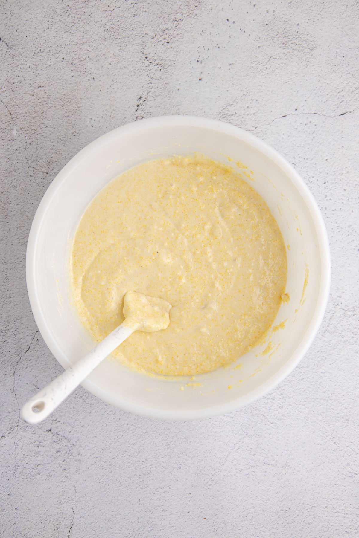 Banana cornbread batter in a bowl with a spoon. 