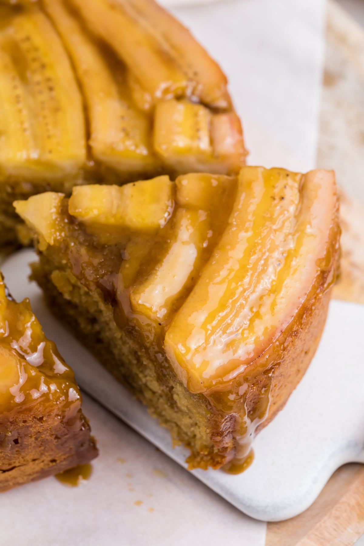 A slice of Banana Upside Down Cake being removed from from a cake on a platter.