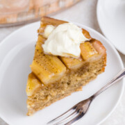 A slice of Banana Upside Down Cake on a plate with a swirl of whipped cream on top.