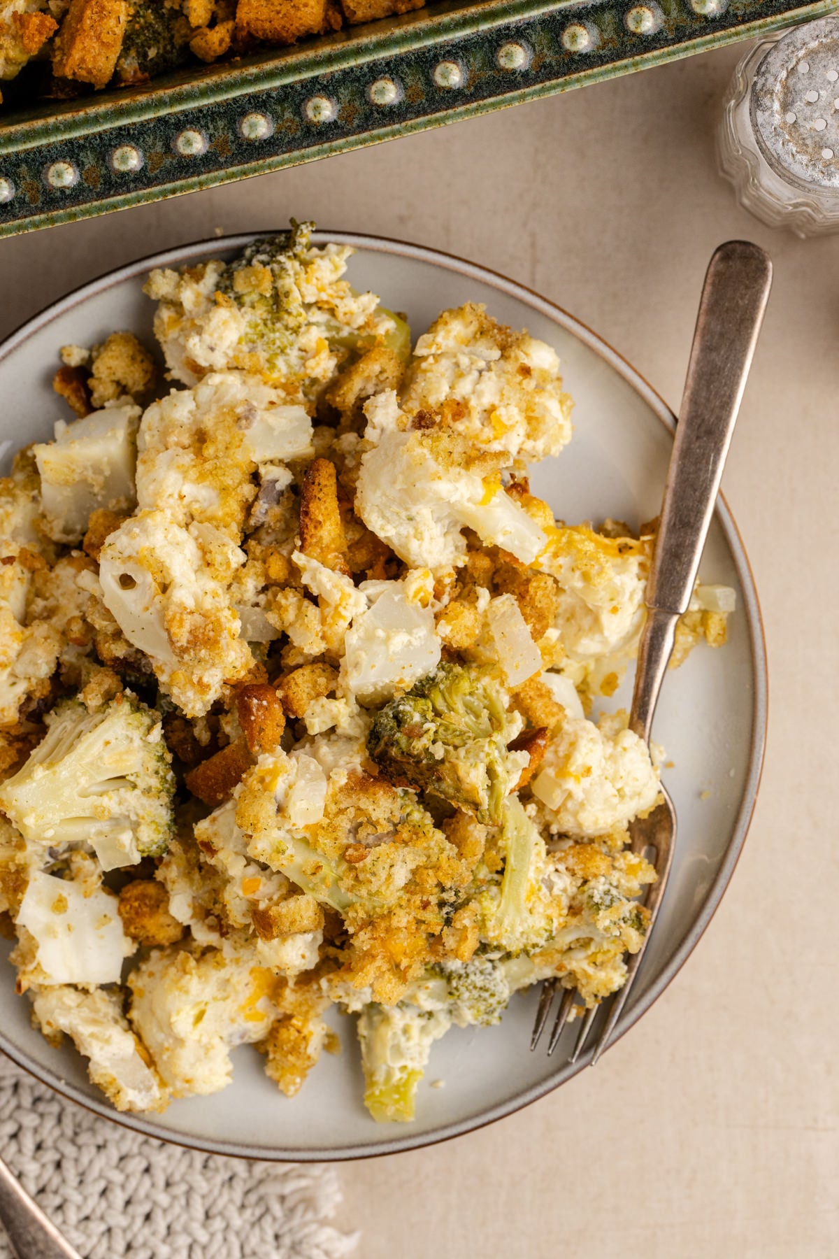A plate full of cauliflower and broccoli casserole on a plate with a fork on the side.