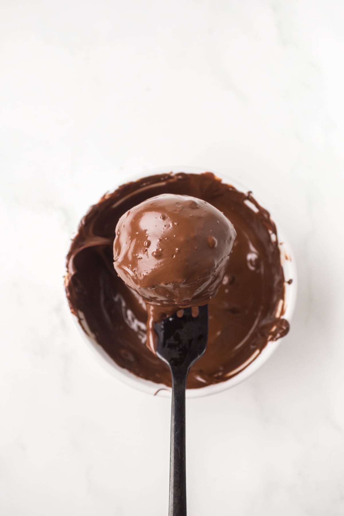 A chocolate chip brownie bite on a fork covered in chocolate ready to be placed on a baking sheet.
