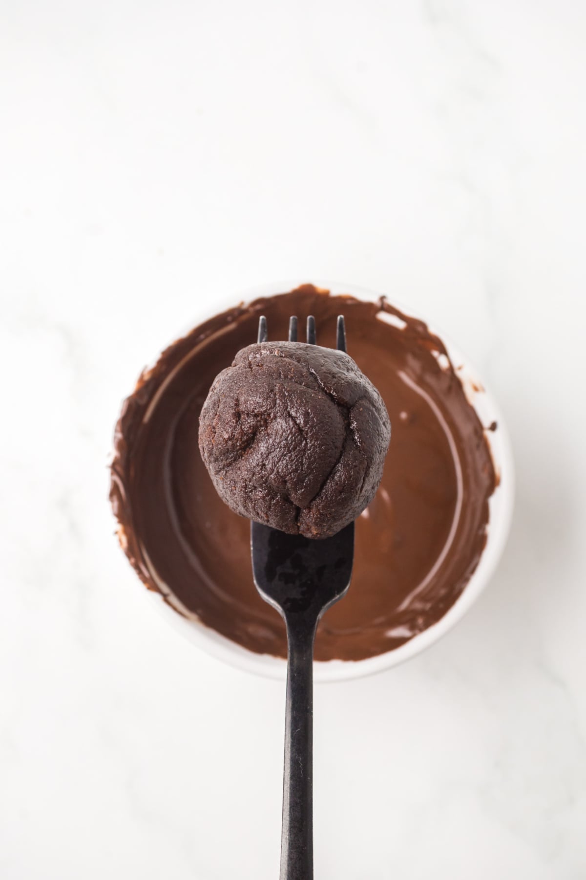 A rolled cookie dough ball surrounded by a brownie bite on a fork ready to be dipped in melted chocolate.