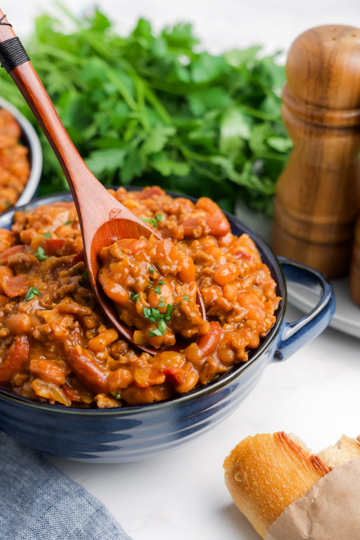 A bowl of baked beans with ground beef with a wooden spoon taking some out.