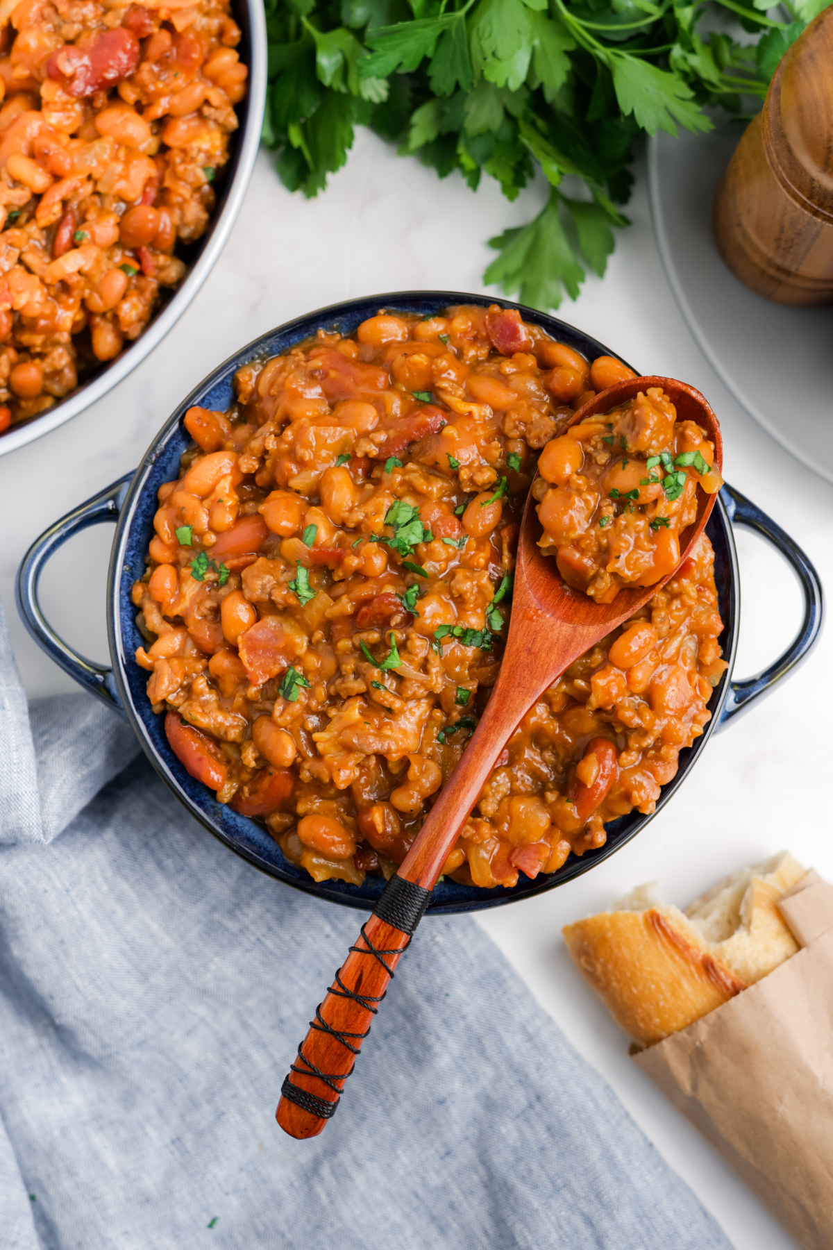 A wooden spoon leaning on the side of a bowl of cowboy baked beans.