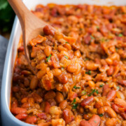 Cowboy baked beans in a casserole dish with a spoon lifting up a serving.