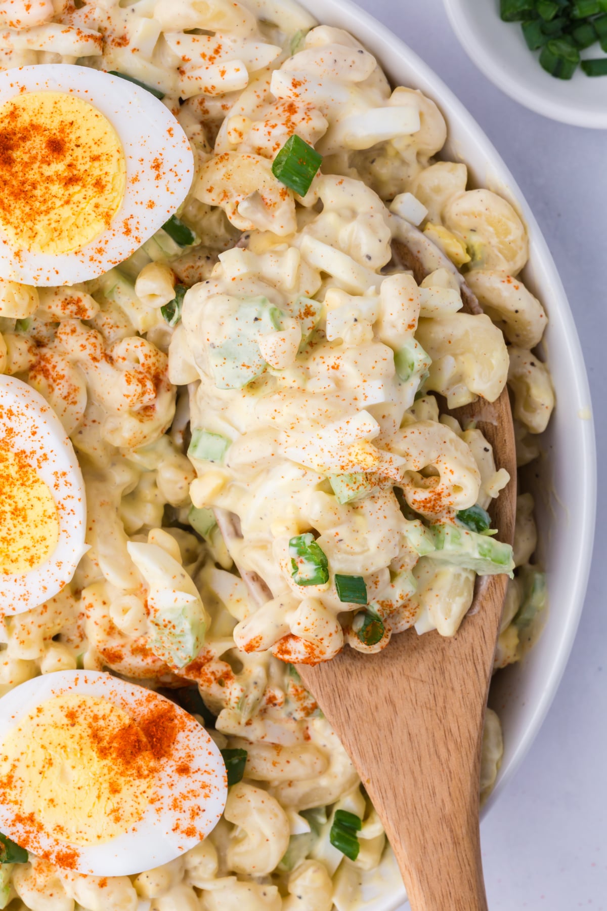 A wooden spoonful of macaroni Salad being lifted out of a bowl.