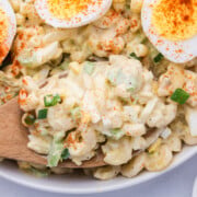 A wooden spoonful of Deviled Egg Macaroni Salad being lifted out of a bowl.