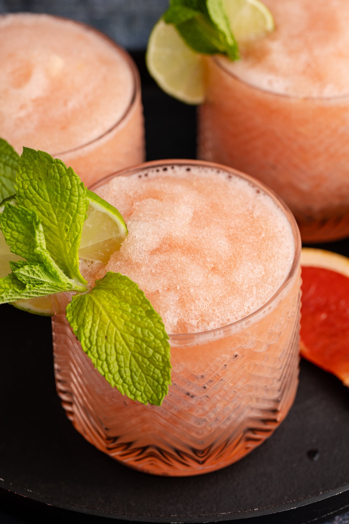 A frozen grapefruit cocktail in a glass with mint and lime to garnish.