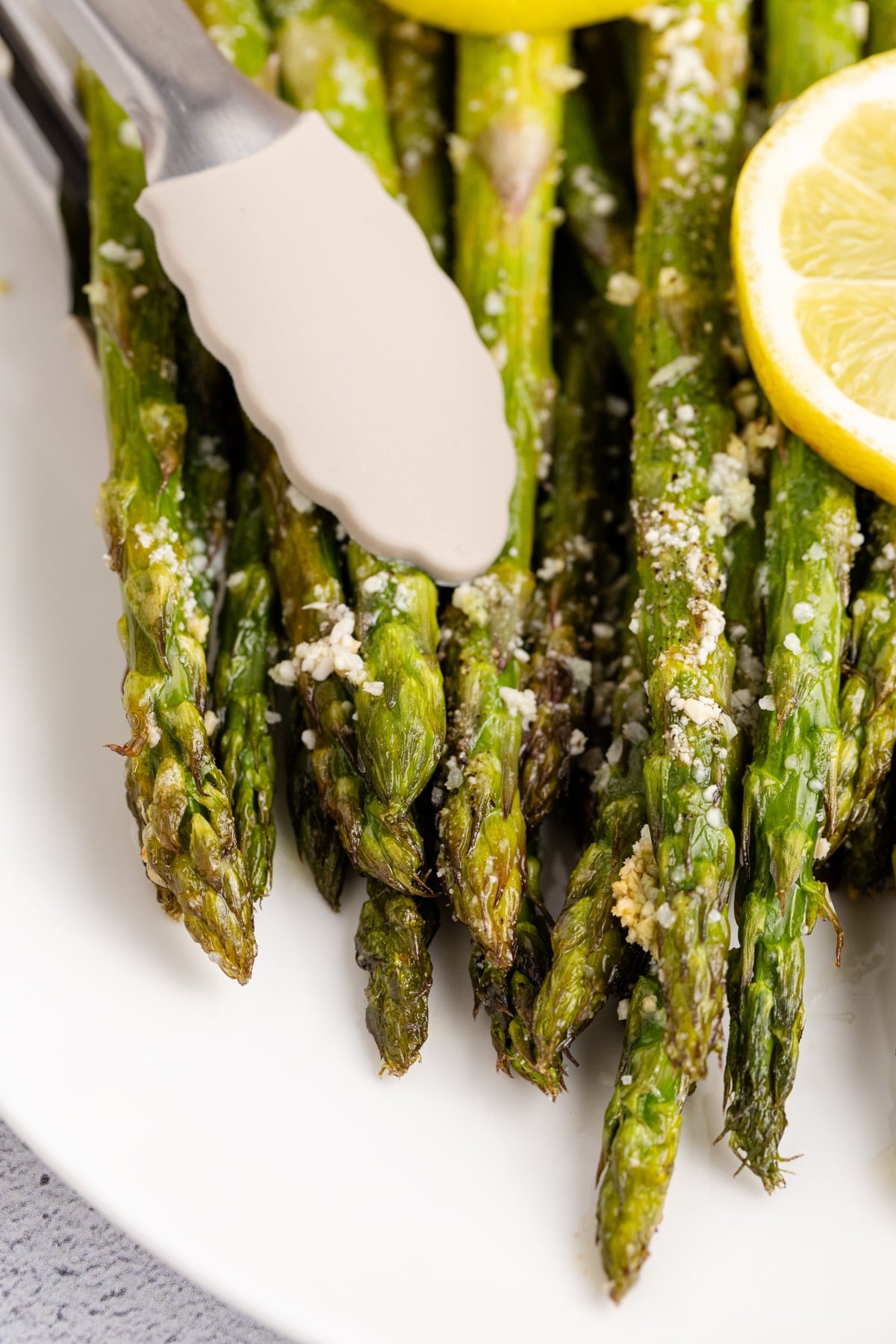 Tongs picking up sheet pan asparagus off a plate.
