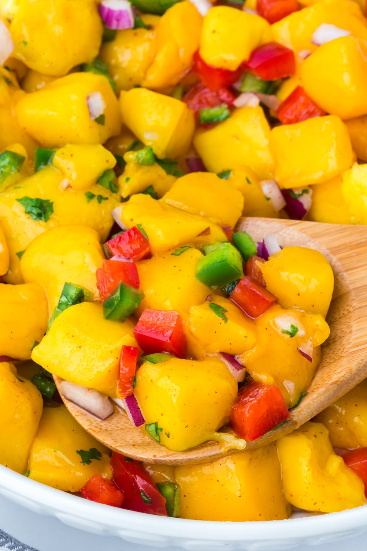 A bowl full of salad and a wooden spoon removing a serving.