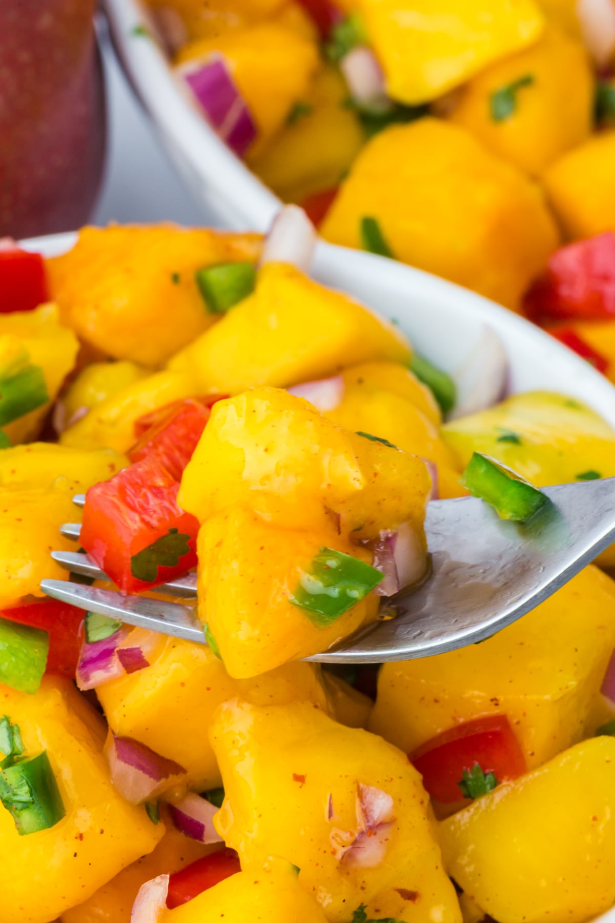 A bowl full of mango salad recipe and a forkful being lifted from bowl.