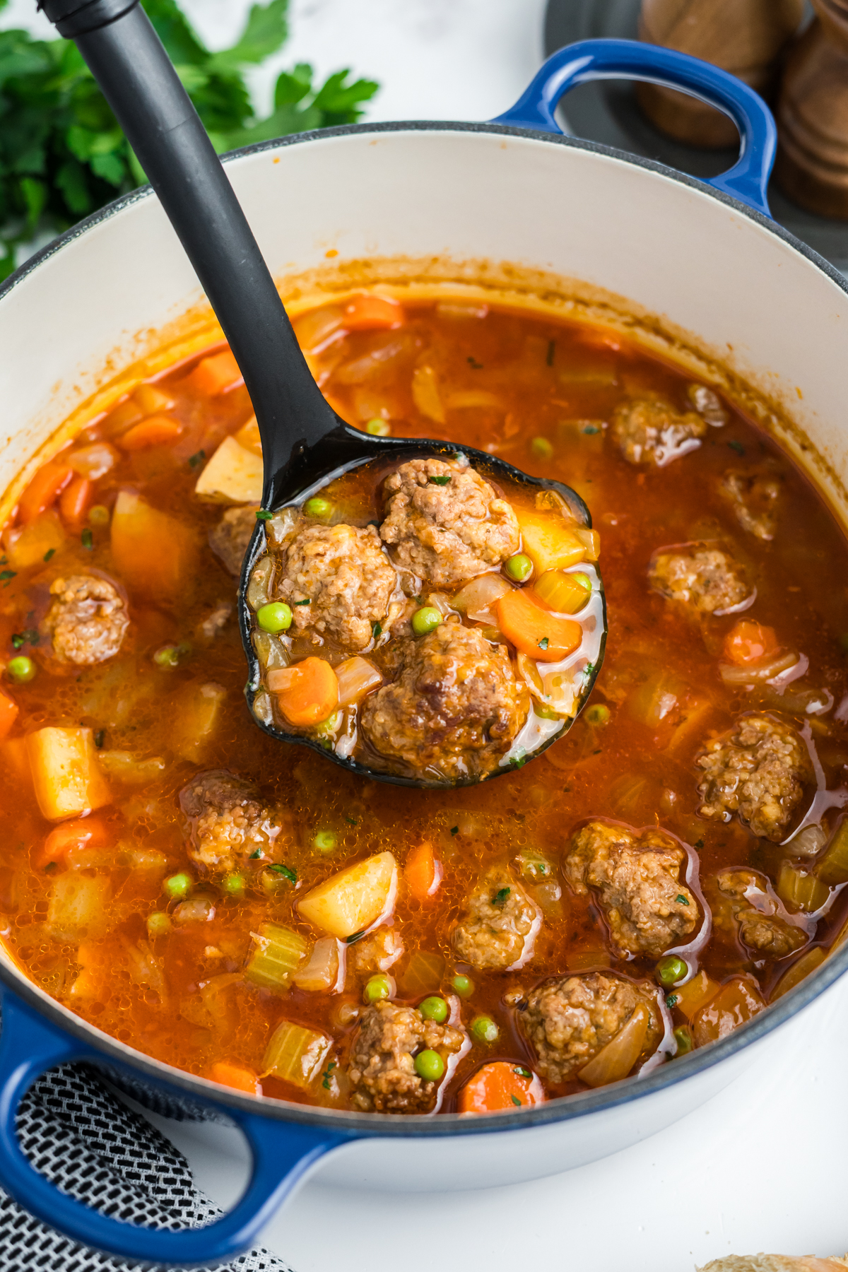 A ladle scooping out some stew with meatballs in it.