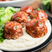 A plate of meatloaf meatballs on mashed potatoes.