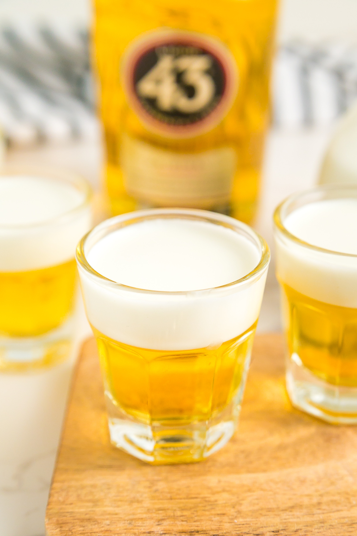 Three shots on a table with a bottle.