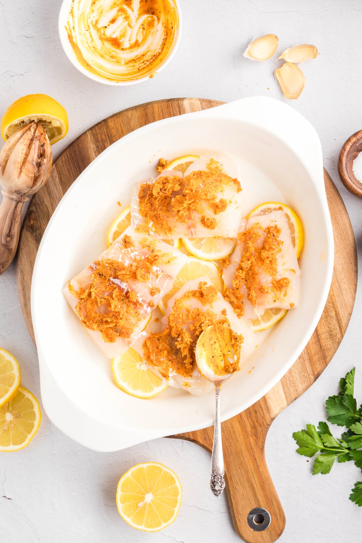 A spoon smearing garlic butter on the top of the fish.