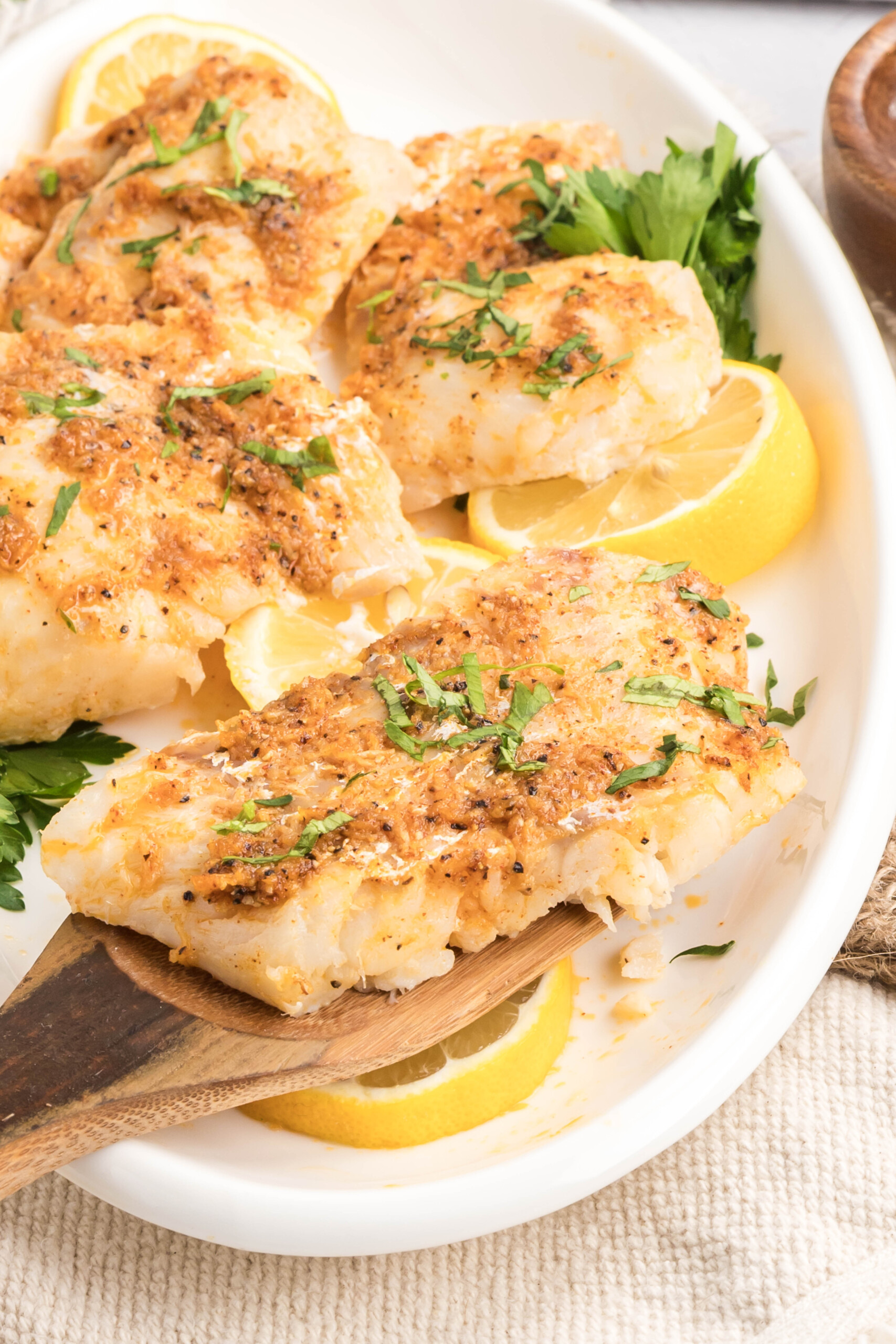 A wooden spatula picking up some haddock filet from the plate.
