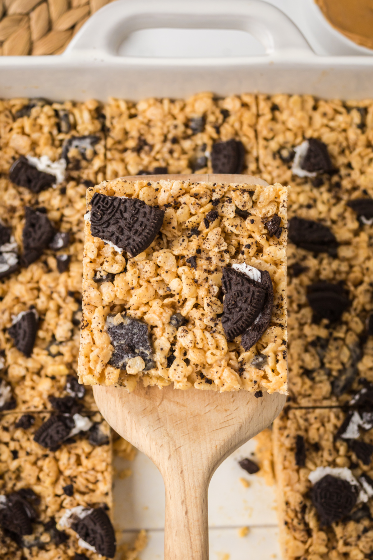 Rice Krispie Treats in a pan with one held in the air above them on a spatula.