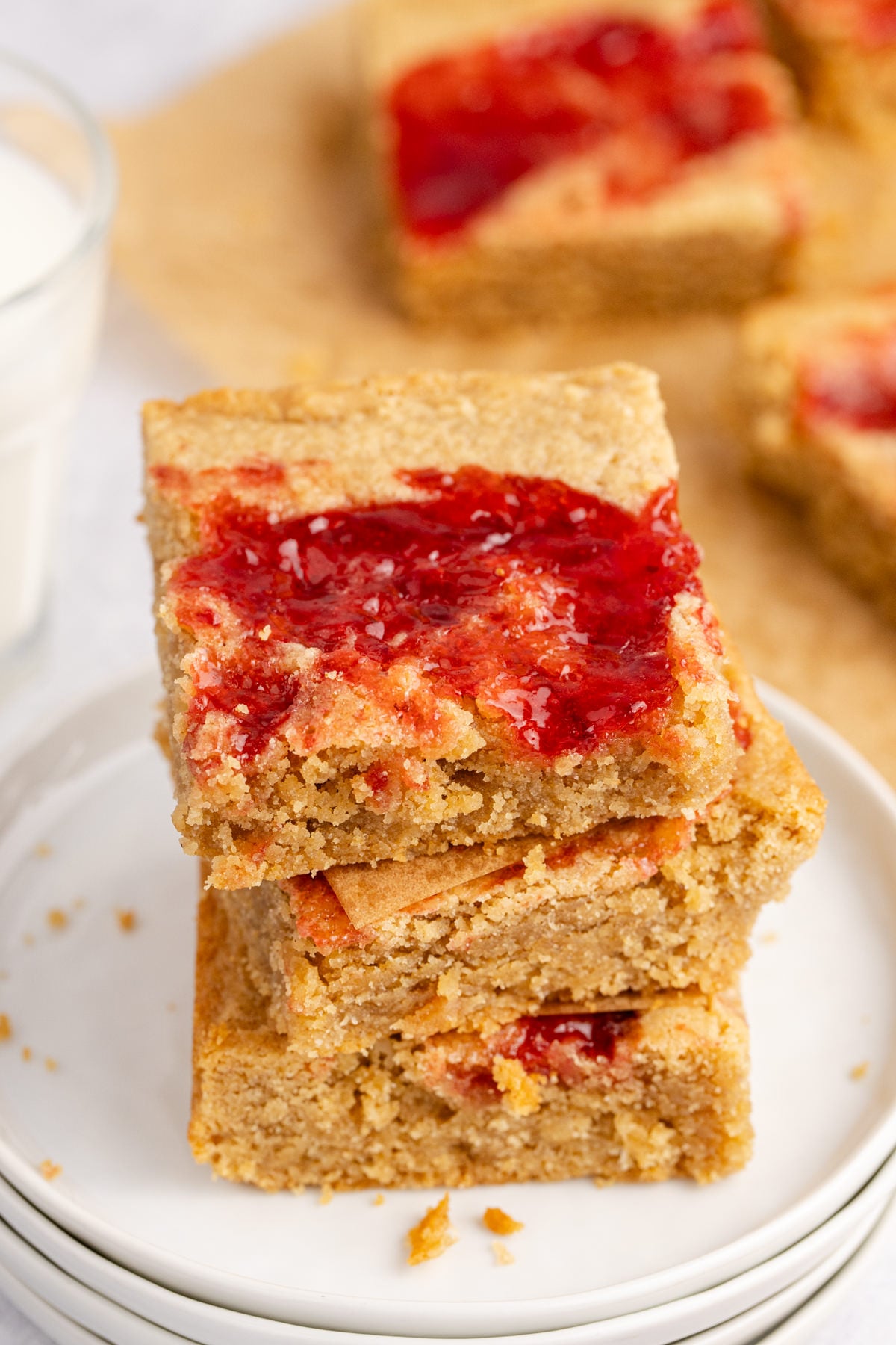 Peanut butter bars with jelly on top stacked on a plate.