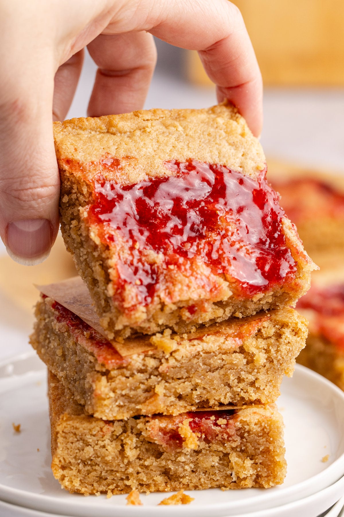A hand picking up and peanut butter and jelly bar from a stack o bars.