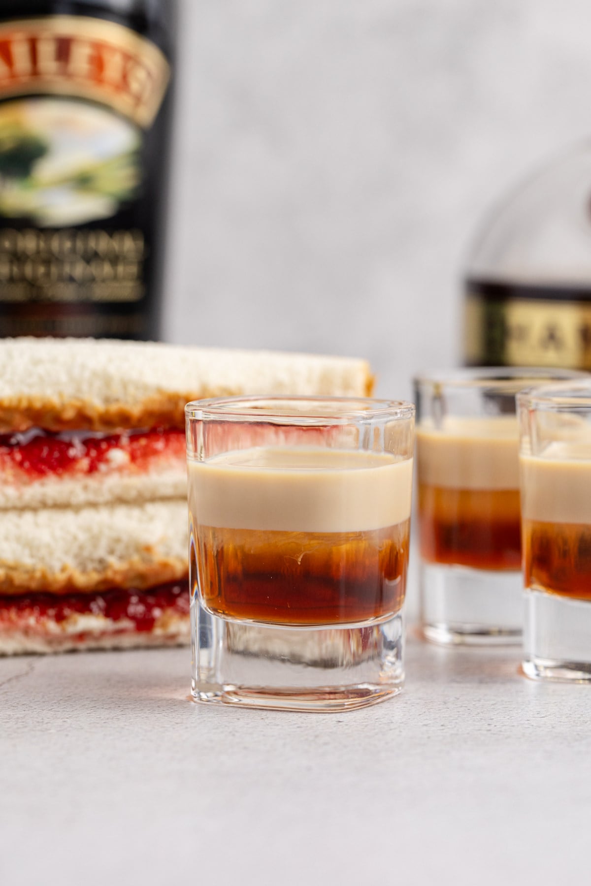 A few shots on a table wiyth a peanut butter and jelly sandwich and a bottle of liqueur.