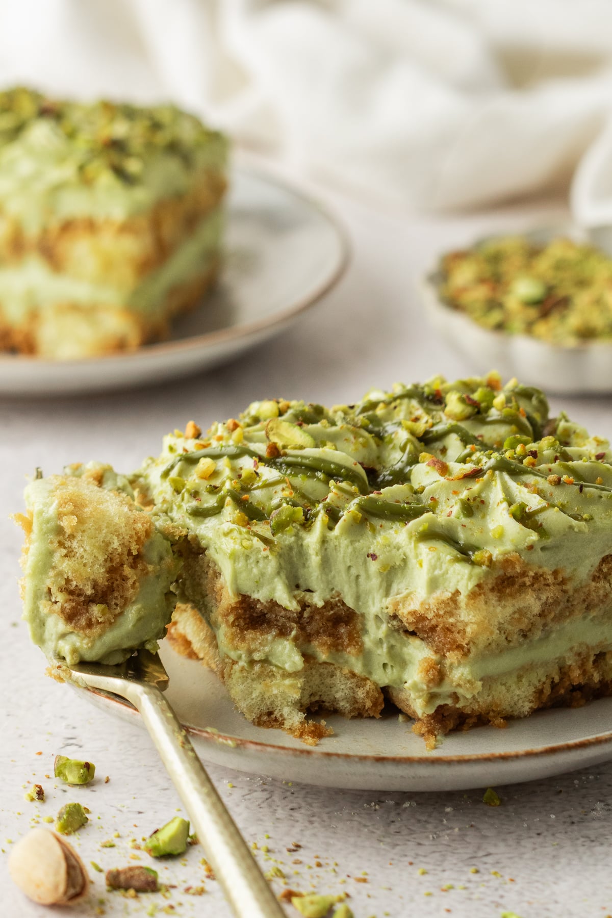 A serving of pistachio tiramisu on a plate with a fork bite missing.