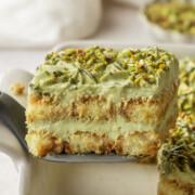 Pistachio tiramisu being lifted out of the dish and held in the air.