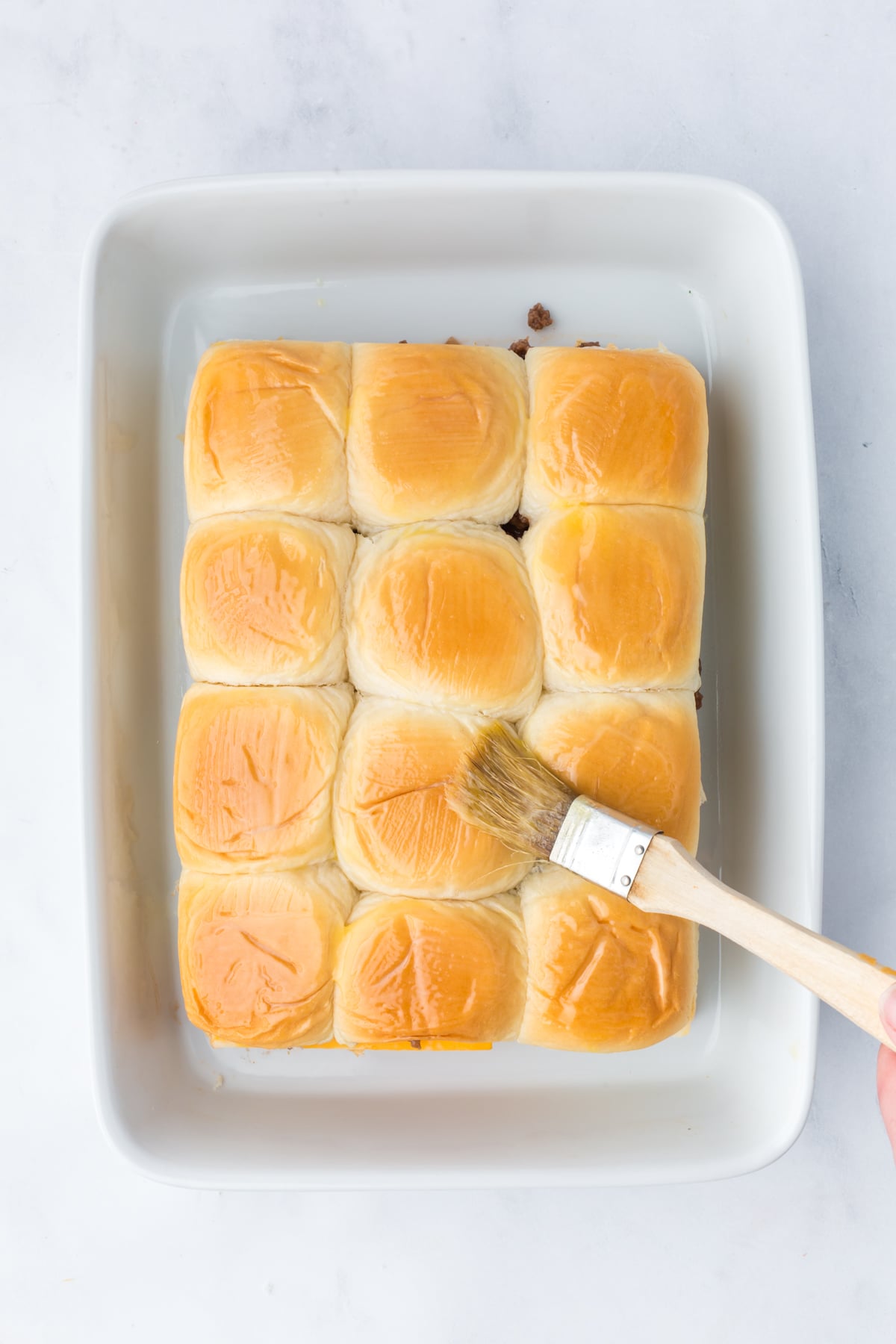 Melted butter being brushed on top of sliders.