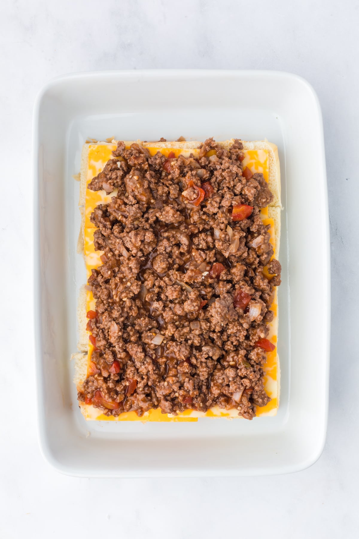 Ground beef mixture added to cheese covered sliders.