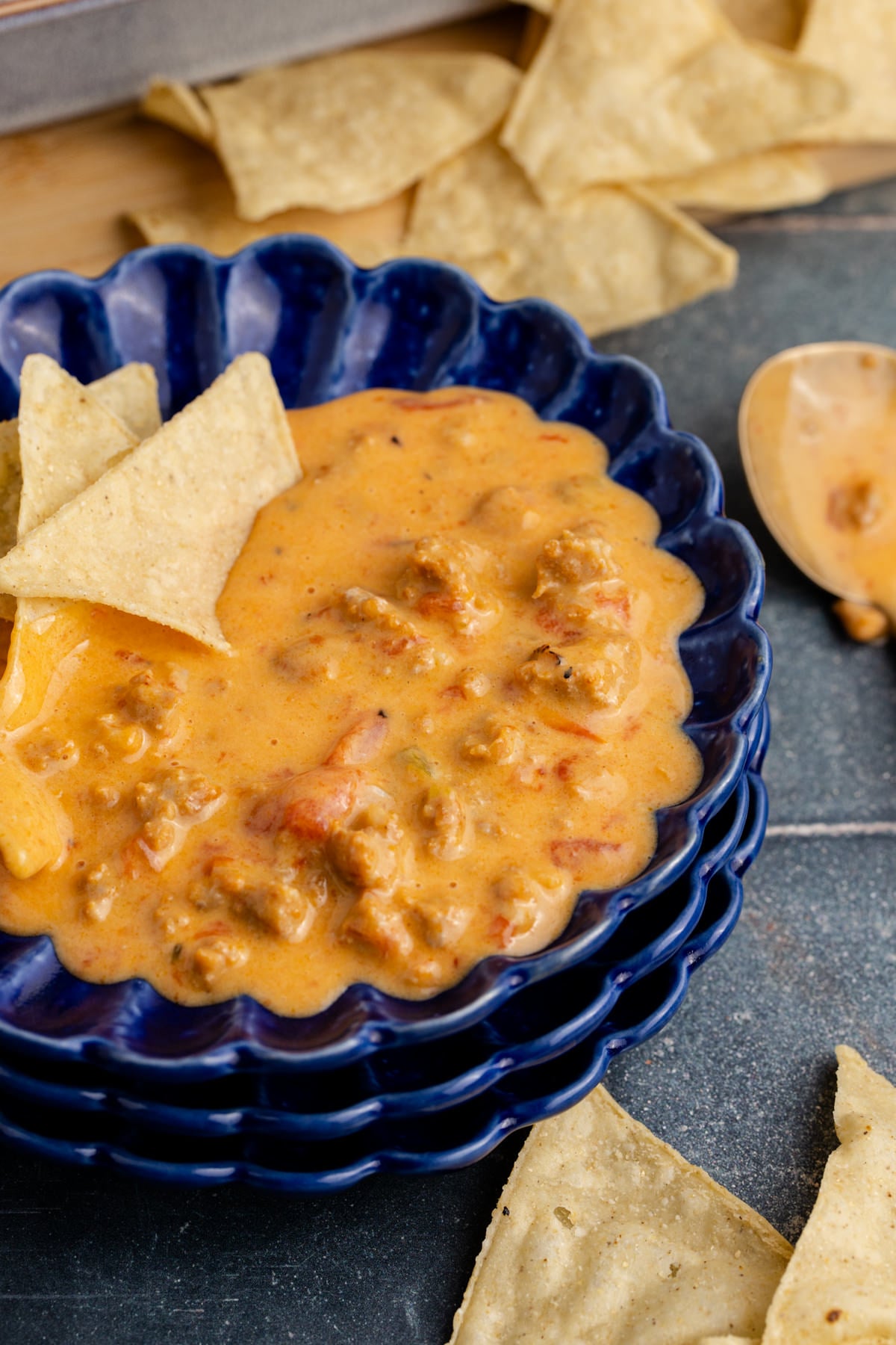A blue bowl with queso dip with chips on the side.