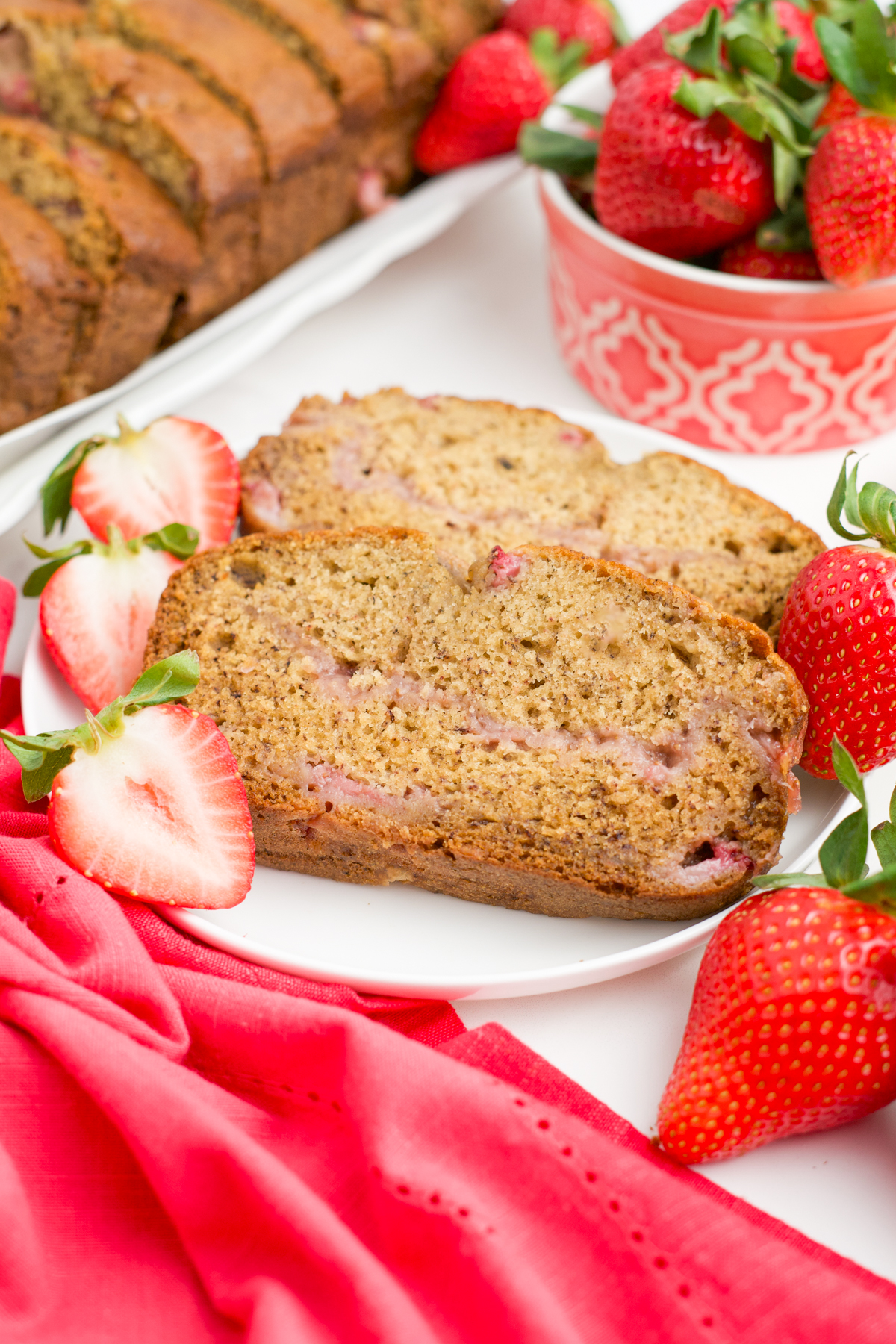 Two slices of Strawberry Banana Bread on a plate with fresh strawberry slices.
