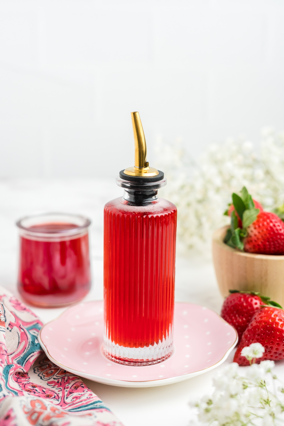 A syrup with strawberries in a glass pourer.