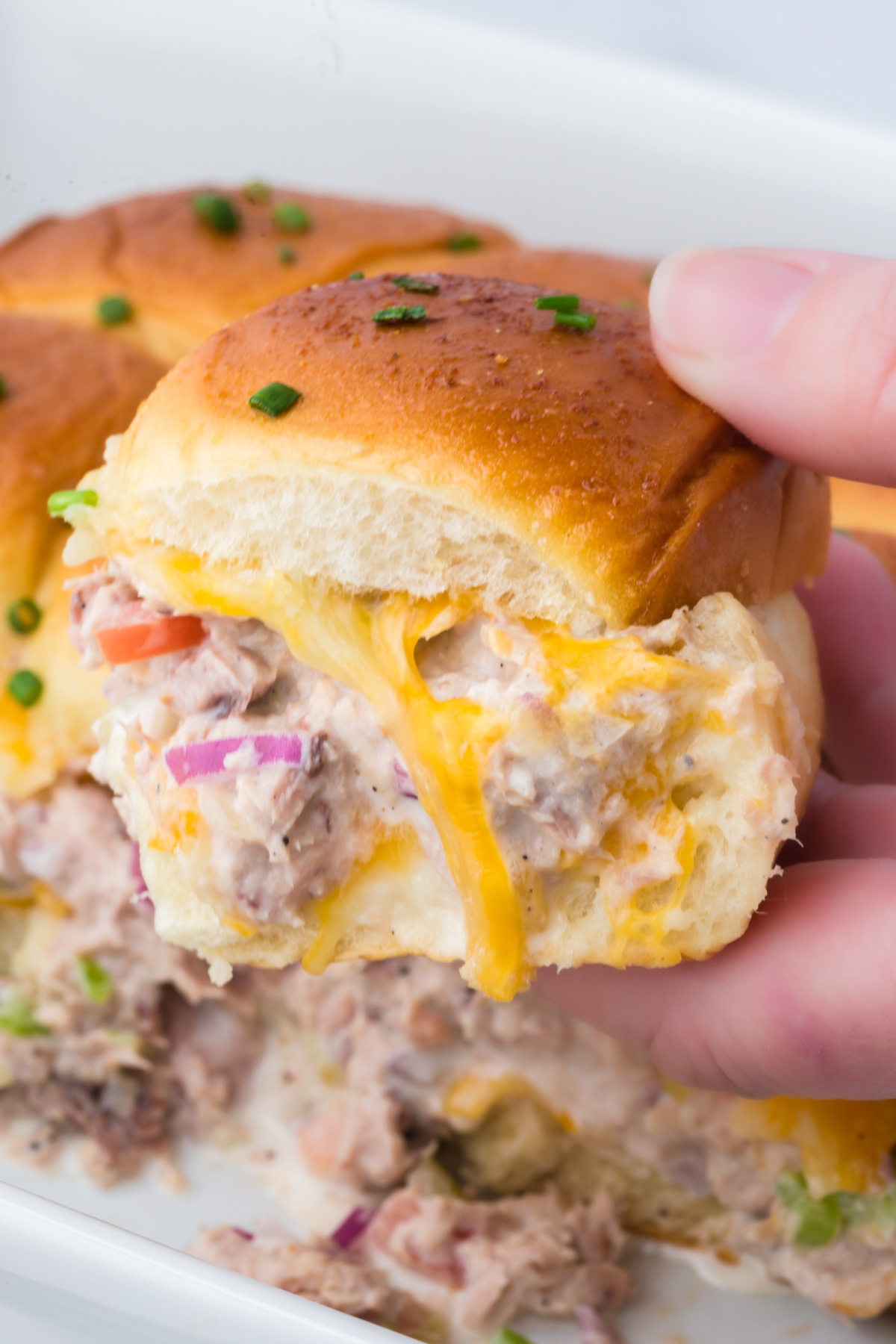 A tuna melt slider held in the air.