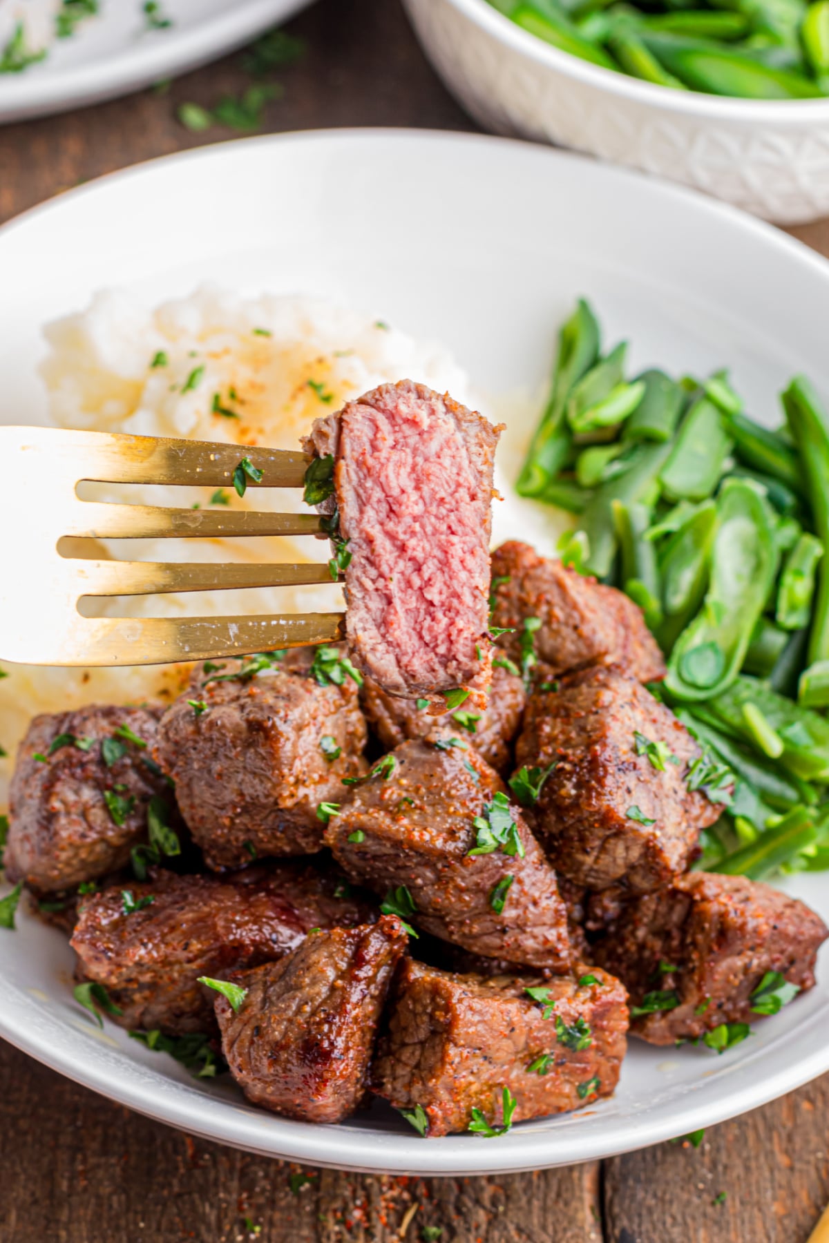 A plate full mashed potatoes, salad and Steak Tips with a piece on a fork on a plate .