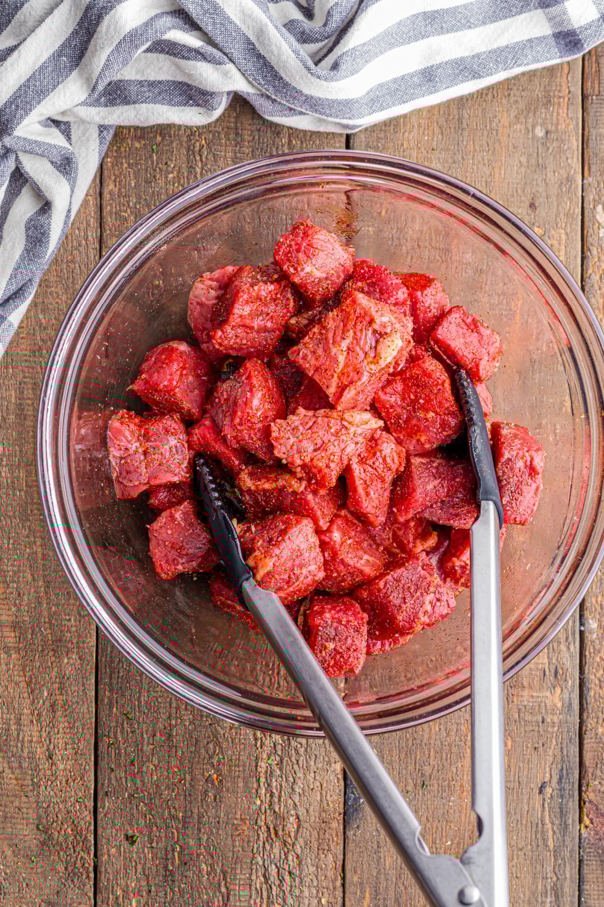 Cut steak pieces being tossed in a bowl using tongs.