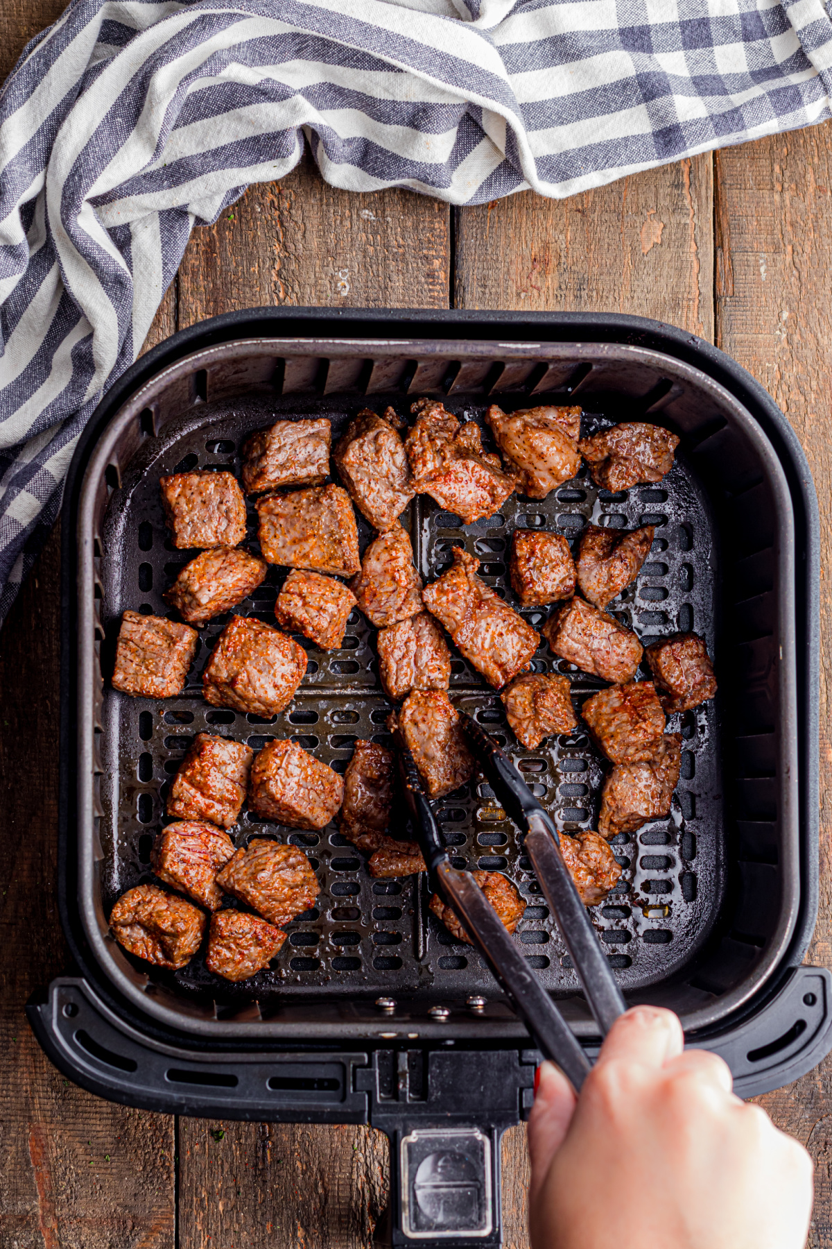 Air fried steak tips being removed from air fryer with tongs.