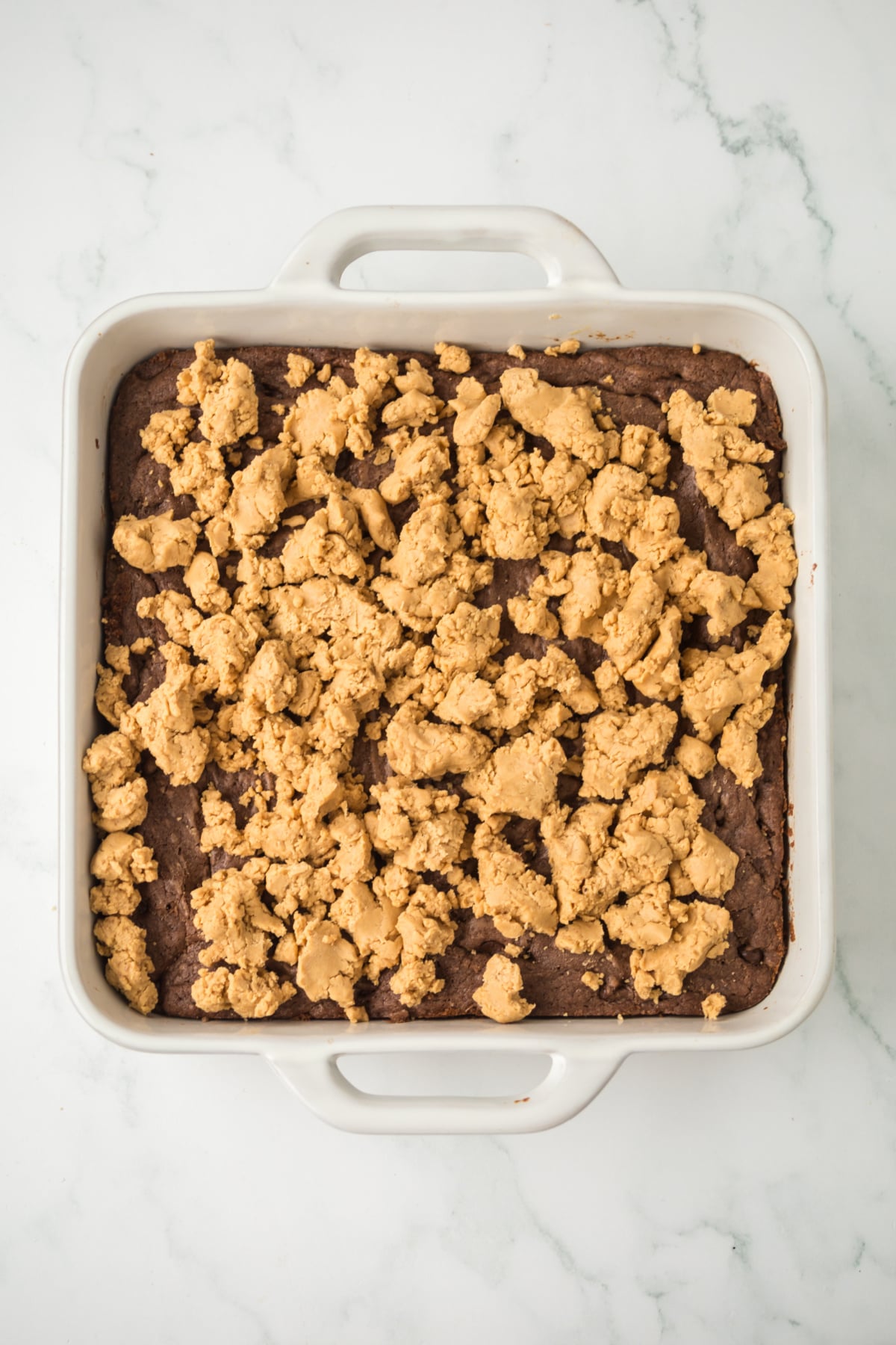 Peanut butter mixture added on top of brownies in pan.