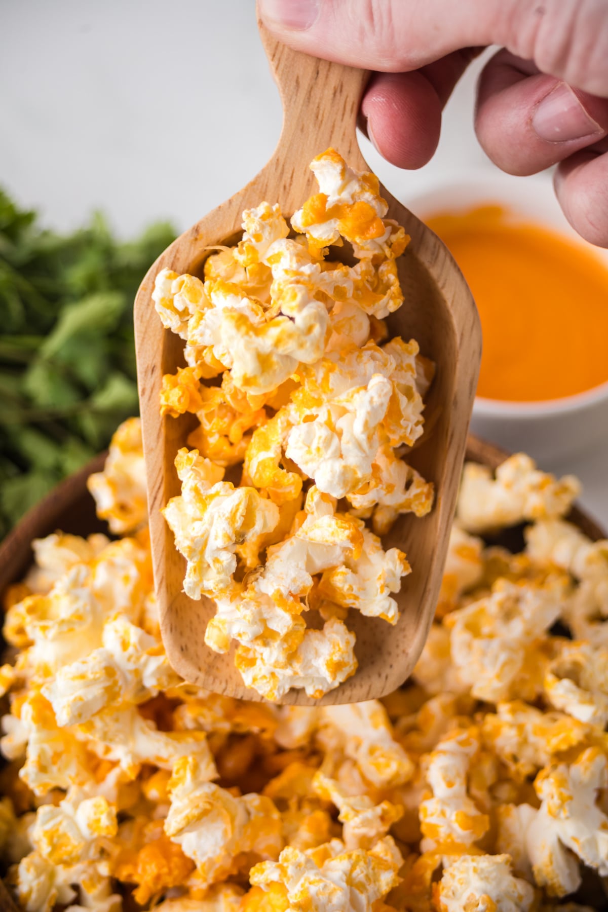 A wooden scoop of popcorn held over a bowlful.