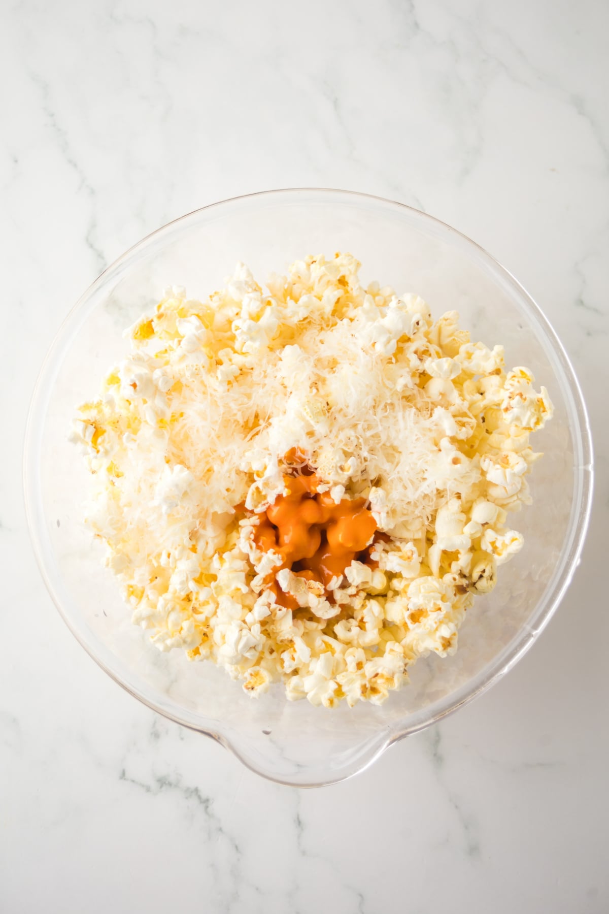 An unmixed bowl of popcorn with parmesan cheese and buffalo sauce.