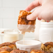 Hawaiian Roll Cinnamon Rolls on a platter with dip in the center and one being dipped.