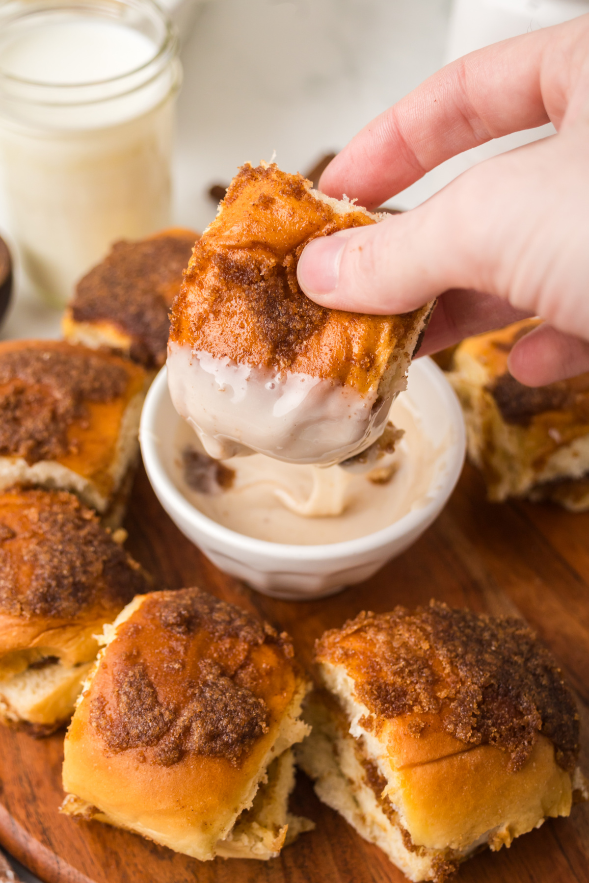 Cinnamon Rolls being dipped in icing surrounded by cinnamon rolls on a platter.